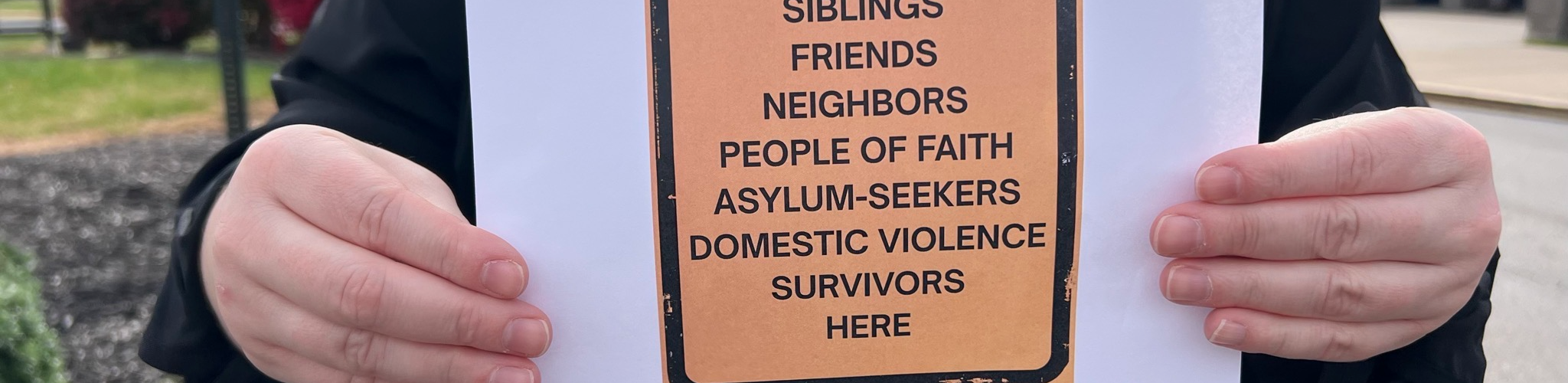 A person in religious garb holds a sign reframing "illegal aliens" into regular human beings.