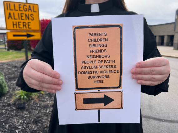 A person in religious garb holds a sign reframing "illegal aliens" into regular human beings.