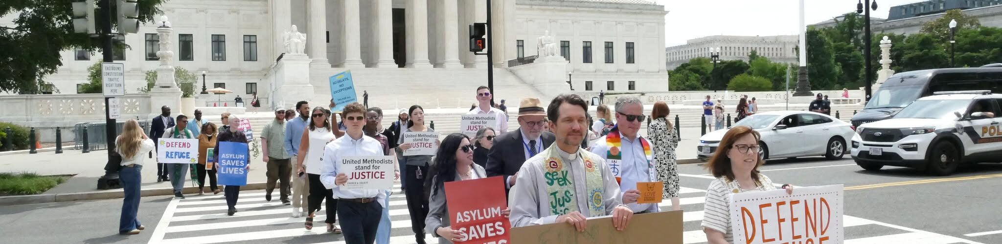 People standing in front of the Supreme Court holding signs and behind a podium