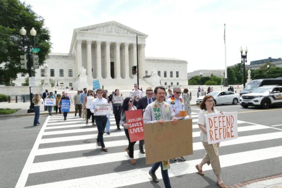 People standing in front of the Supreme Court holding signs and behind a podium